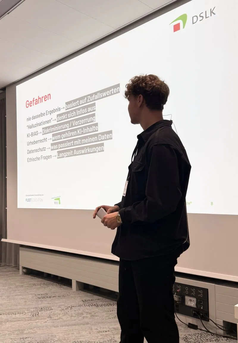 Anton Luków steht vor einer großen Leinwand mit DSLK-Logo und der Folie „Gefahren“ zu Halluzinationen, KI-Bias, Urheberrecht, Datenschutz und ethischen Fragen